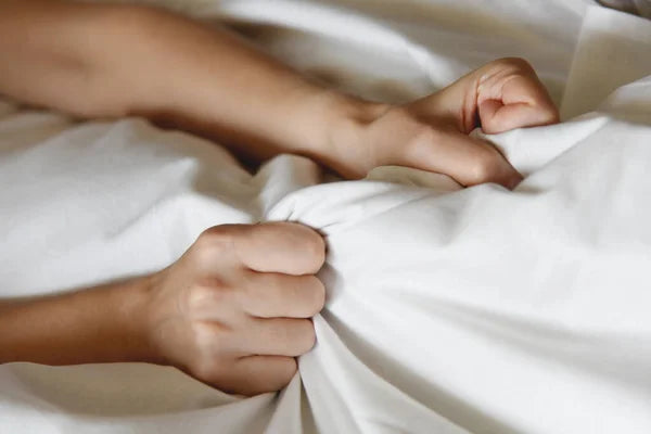 Hands gripping a white bedsheet, illustrating excitement related to how to squirt with a vibrator.