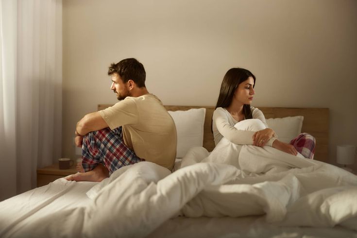 Couple sitting apart on bed, symbolizing emotional distance and decline in sexual life decline.
