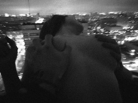 Two people embracing against a blurred city skyline at night in black and white