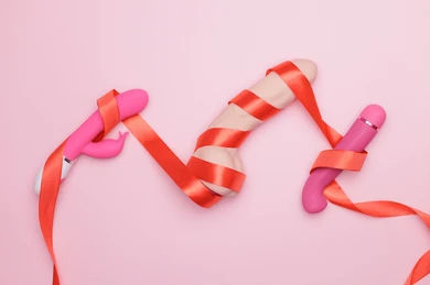 Three vibrators wrapped in red ribbons on a pink background, showcasing variety and playfulness of vibrators.