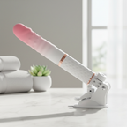 Pink White Grad Mini Thruster 10-Speed Auto App Smart Dildo for Women on a marble countertop with towels and a plant.
