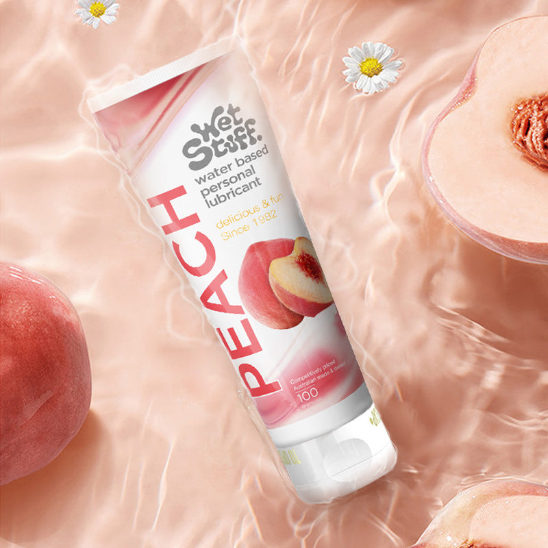 Wet Stuff Peach Water-Based Personal Lubricant floating on water with fresh peaches and flowers - Sweet peach flavored silky lubricant