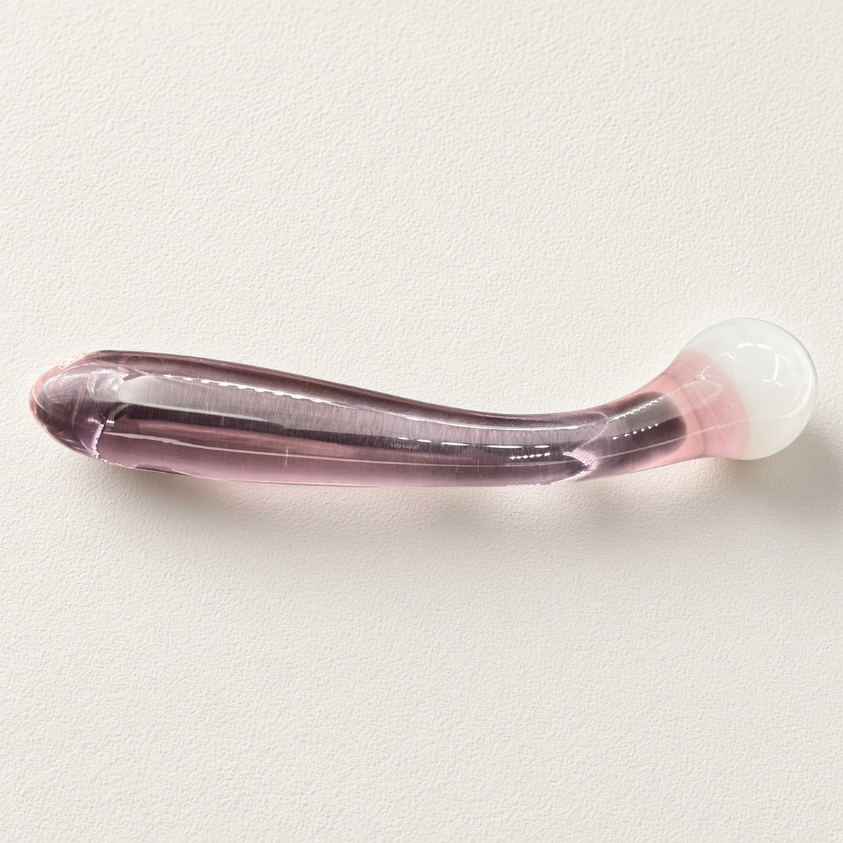 Curved pink glass dildo with rounded white ball head on a light background