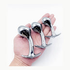 Hand holding small medium and large silver curved aluminum anal plugs for size reference