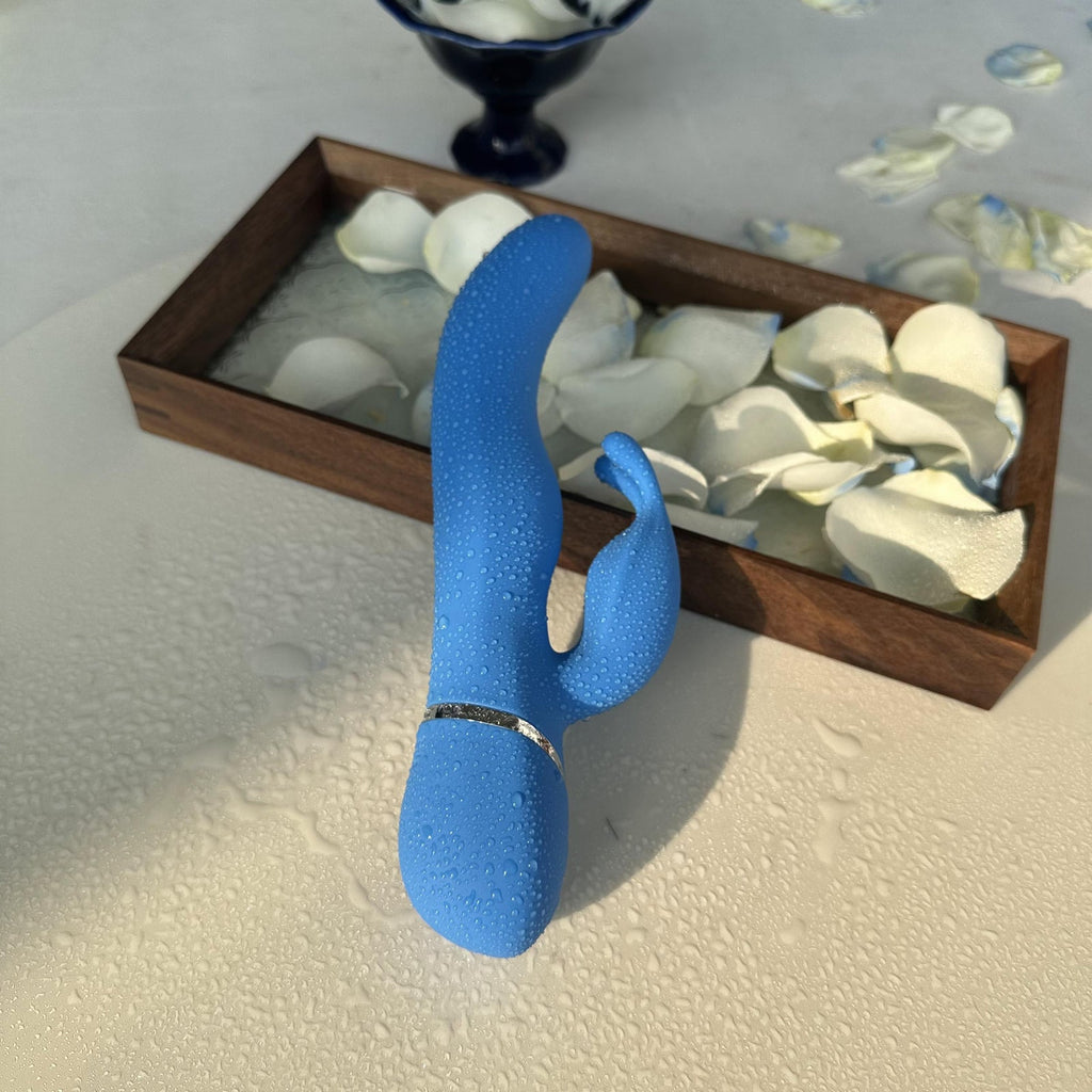 Waterproof blue rabbit vibrator upright with water droplets and petals